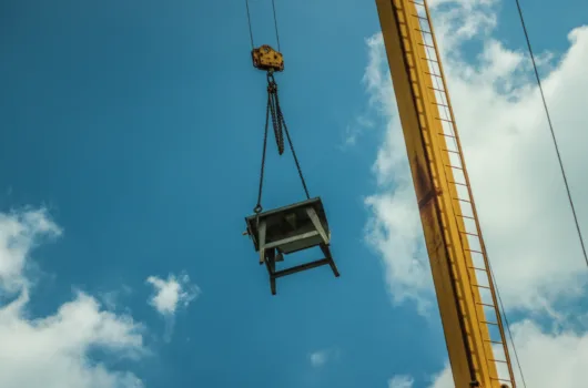 Guindaste realizando o içamento de carga pesada em ambiente industrial sob céu azul.