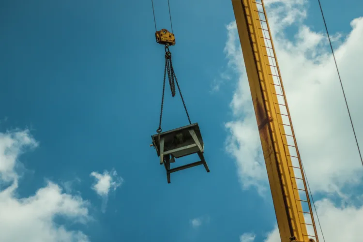 Guindaste realizando o içamento de carga pesada em ambiente industrial sob céu azul.
