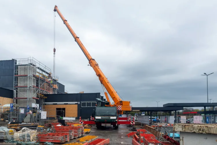 Guindaste telescópico realizando içamento em obra de construção civil com estrutura metálica e materiais no canteiro