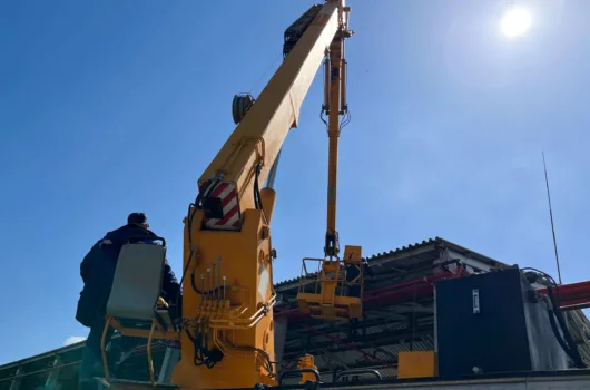 Guindaste hidráulico operando em área industrial com operador qualificado durante operação de içamento